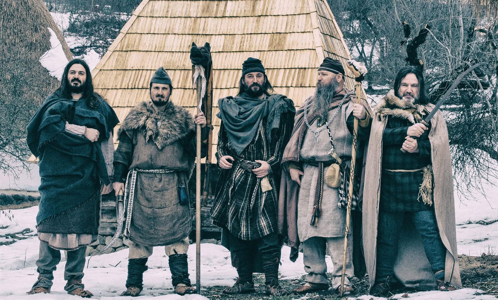 Membri Omnis Barbaria în costume antice, iarna, în fața unei case din lemn